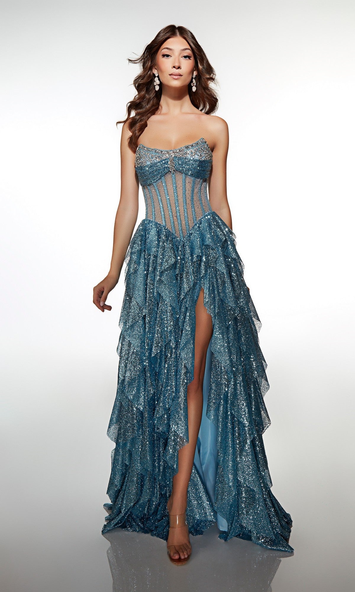 A woman poses against a white background in the Alyce 62081 Long Formal Dress, featuring a light blue, glittery strapless design with a sheer bodice, layered ruffle skirt, and high slit.